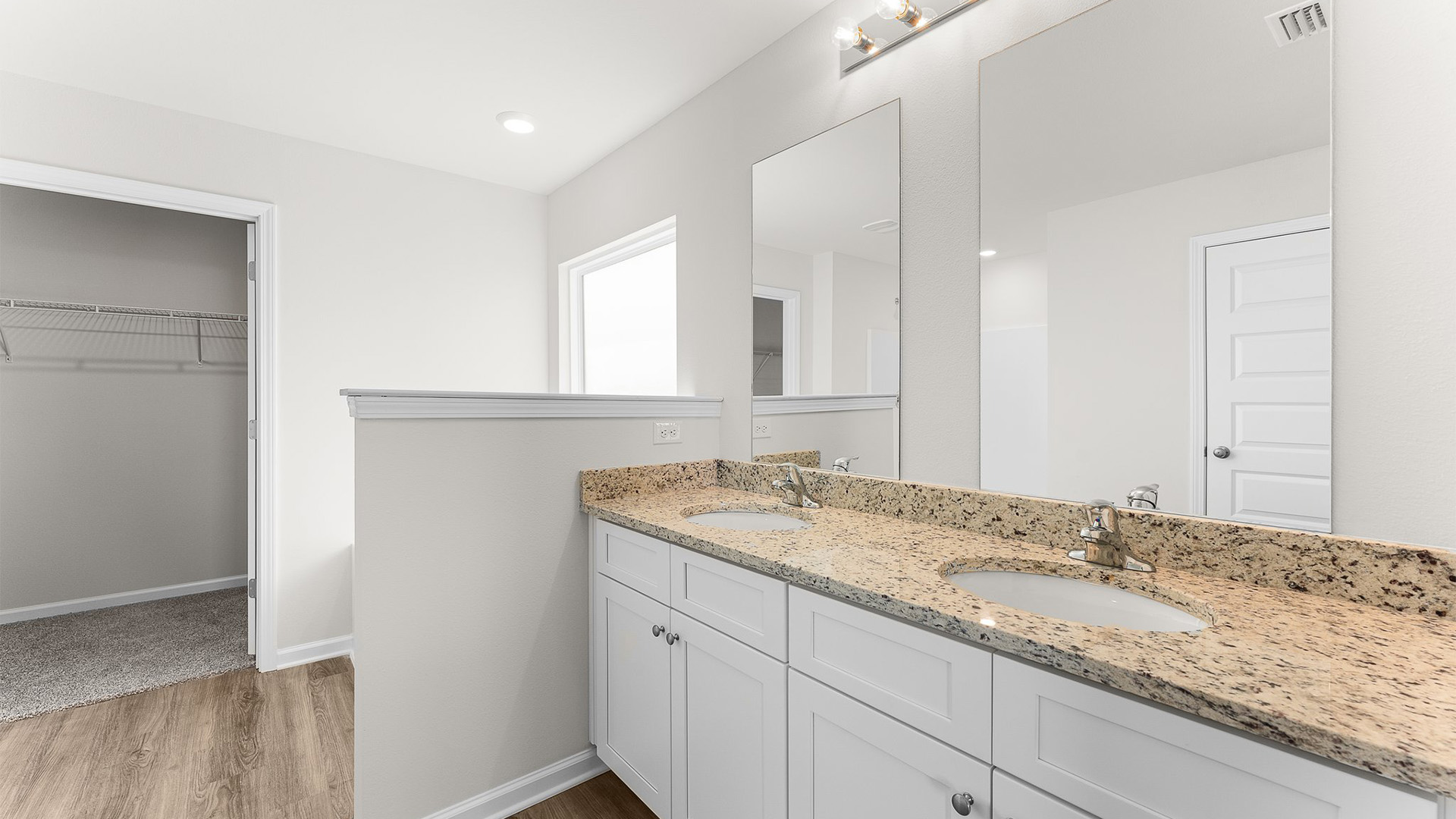 Primary bathroom with double vanity white cabinets and granite countertops and EVP flooring and tub and window.