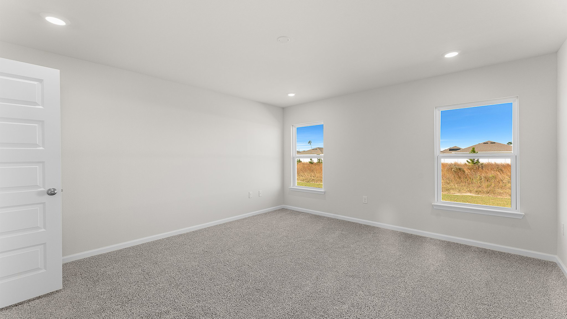 Primary bedroom with carpet floors and two windows.