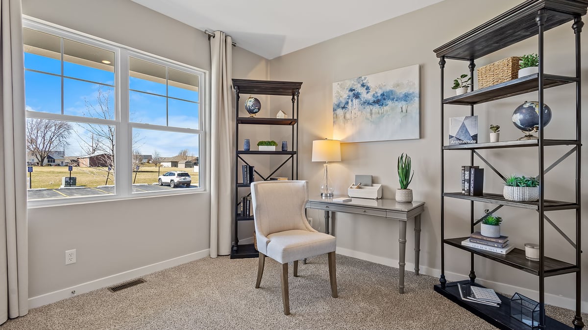 Front bedroom staged as an office space with carpeted floors and a big window.