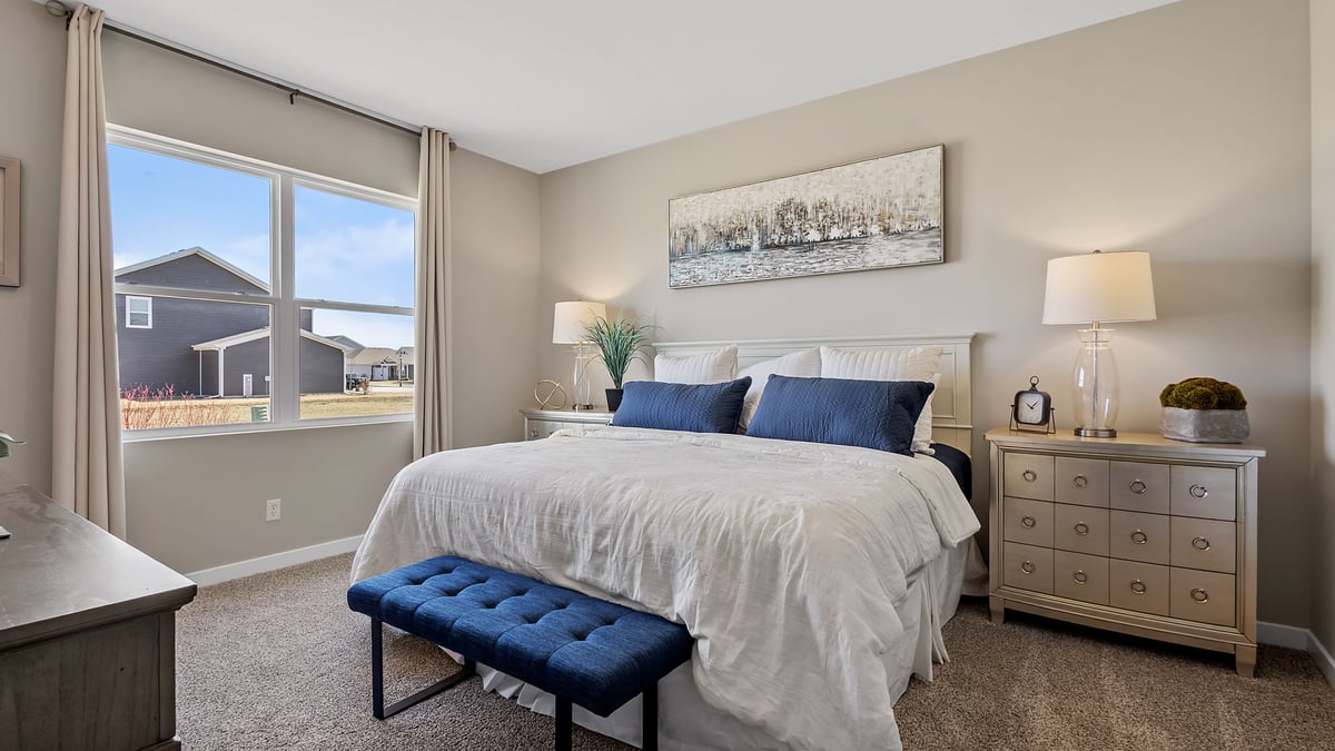 Primary bedroom with a big window and carpeted floors.
