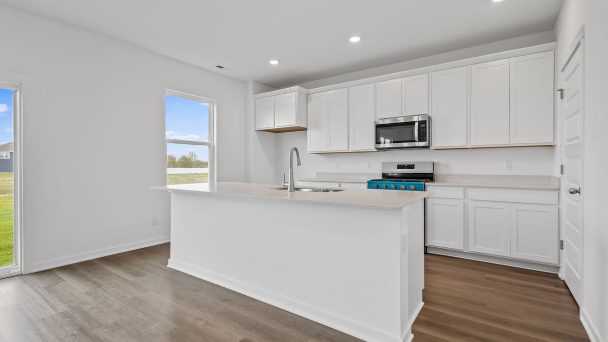 Kitchen with white cabinetry and windows with island and open layout.