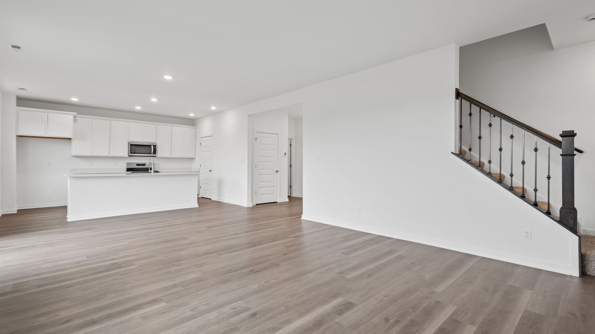 Open living room with view of kitchen and open brown railing on staricase.