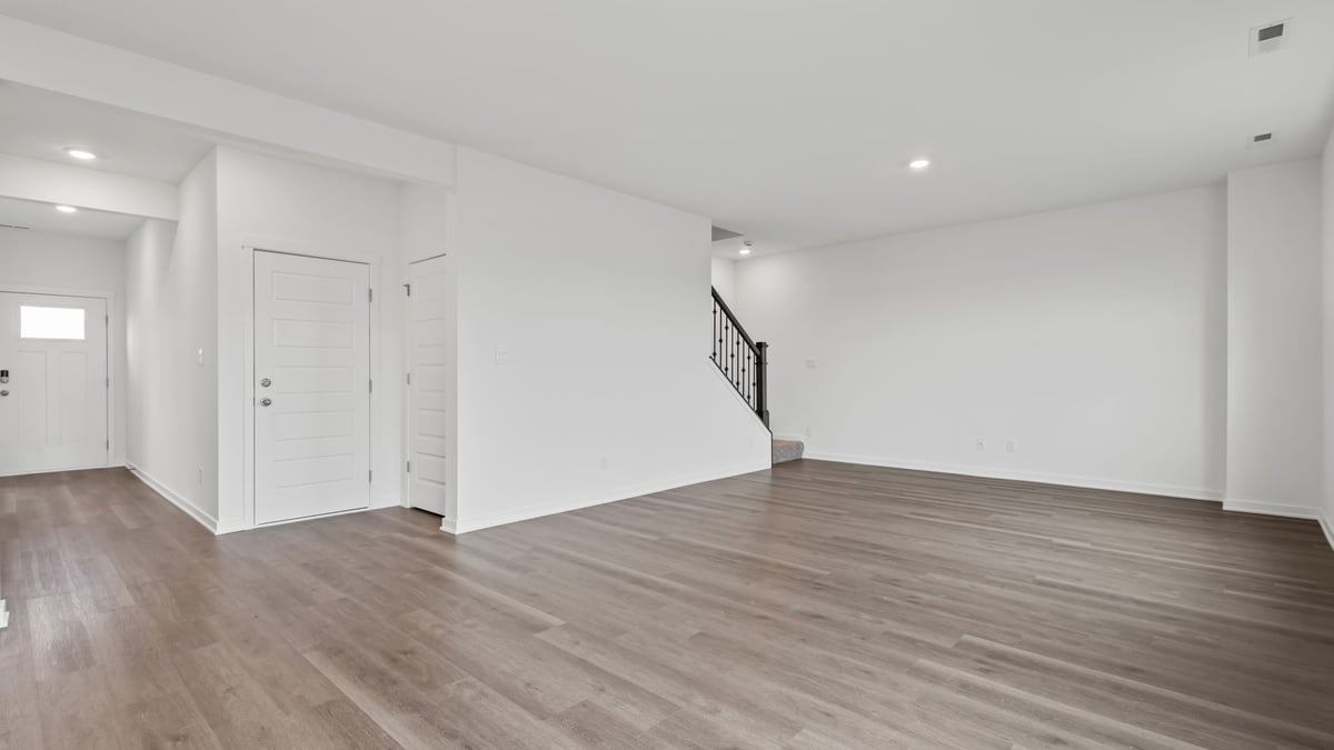 Open living room with view of front door and open brown staircase.