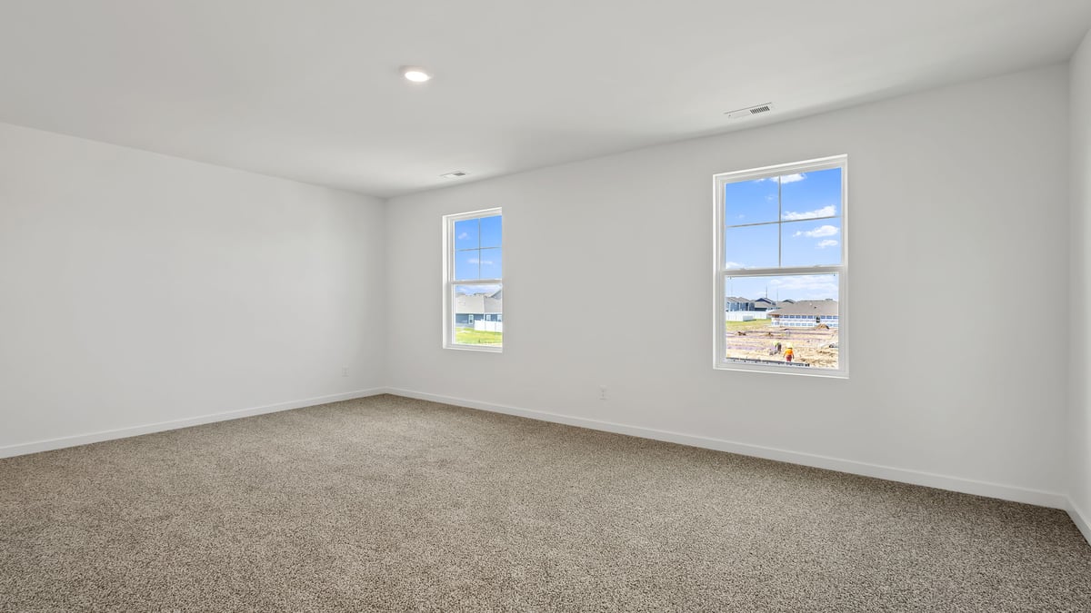 Primary bedroom with carpeted floors and two windows.
