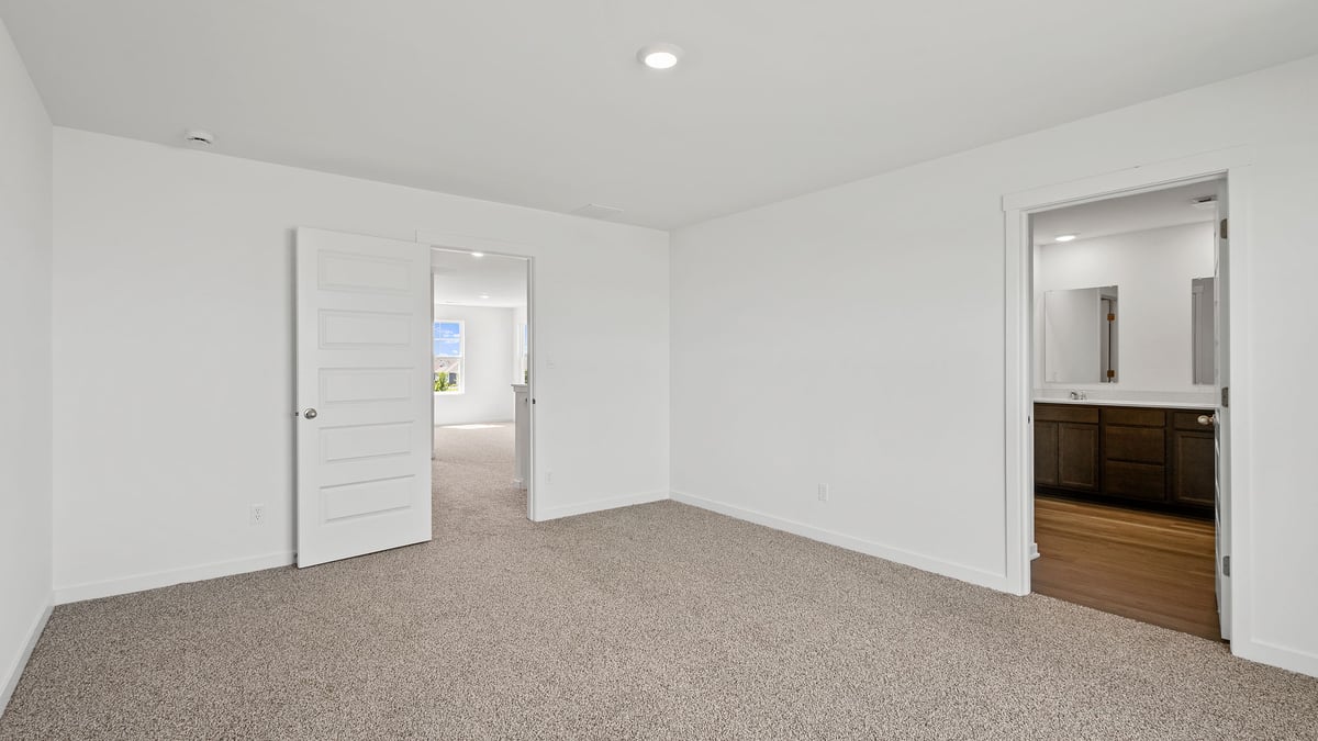 Primary bedroom with carpeted floors and own primary bathroom.
