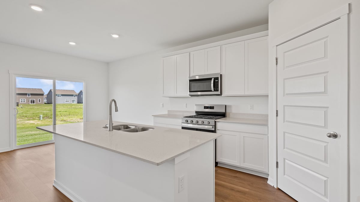 Kitchen with white cabinetry with island and dining area with sliding glass door.