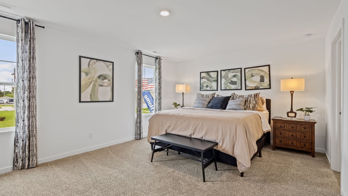 Primary bedroom with carpeted floors and two large windows.