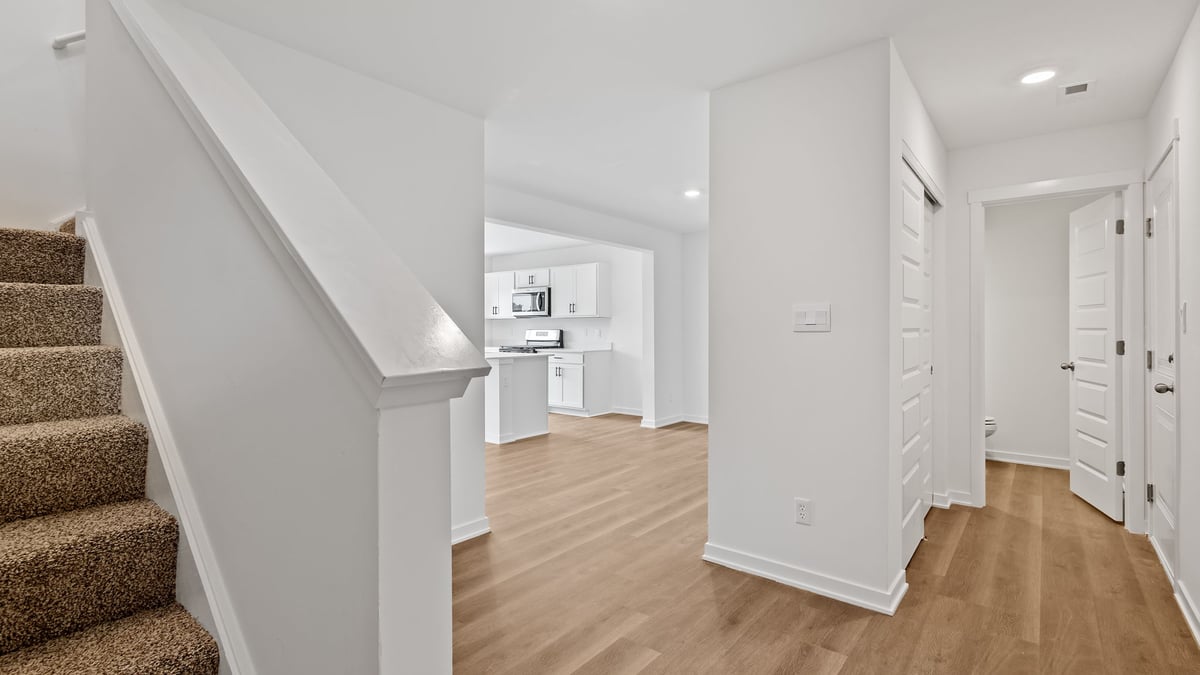 Hallway with hard wood floors and view of carpeted staircase.