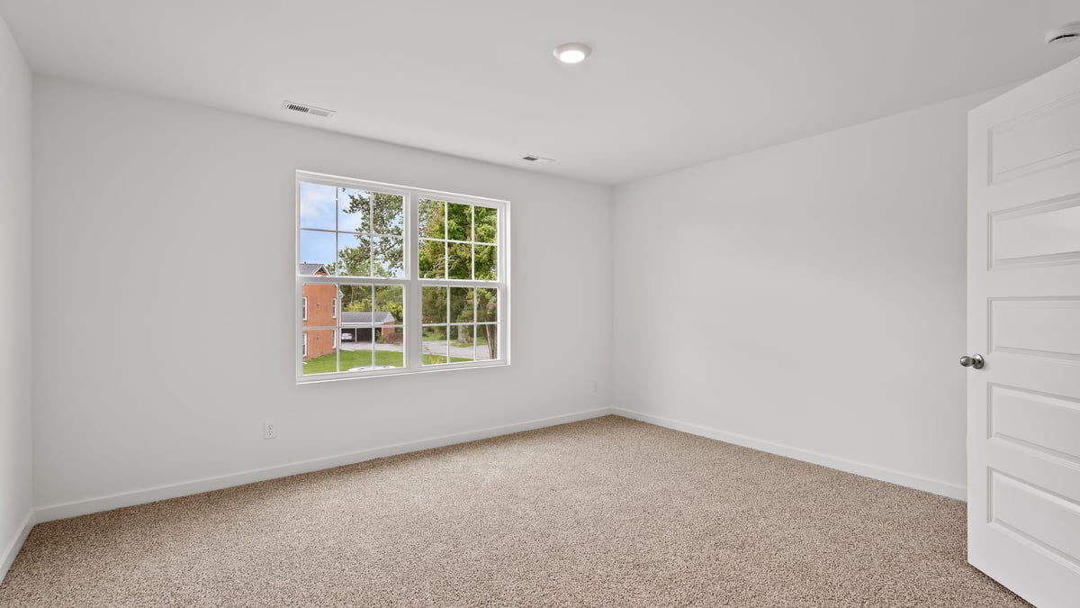 Primary bedroom with carpeted floors with a big window and plenty of space.