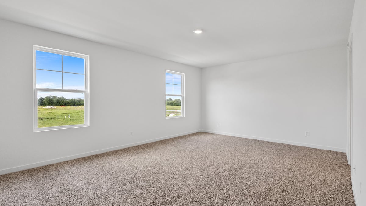 Primary bedroom with carpet and two windows.