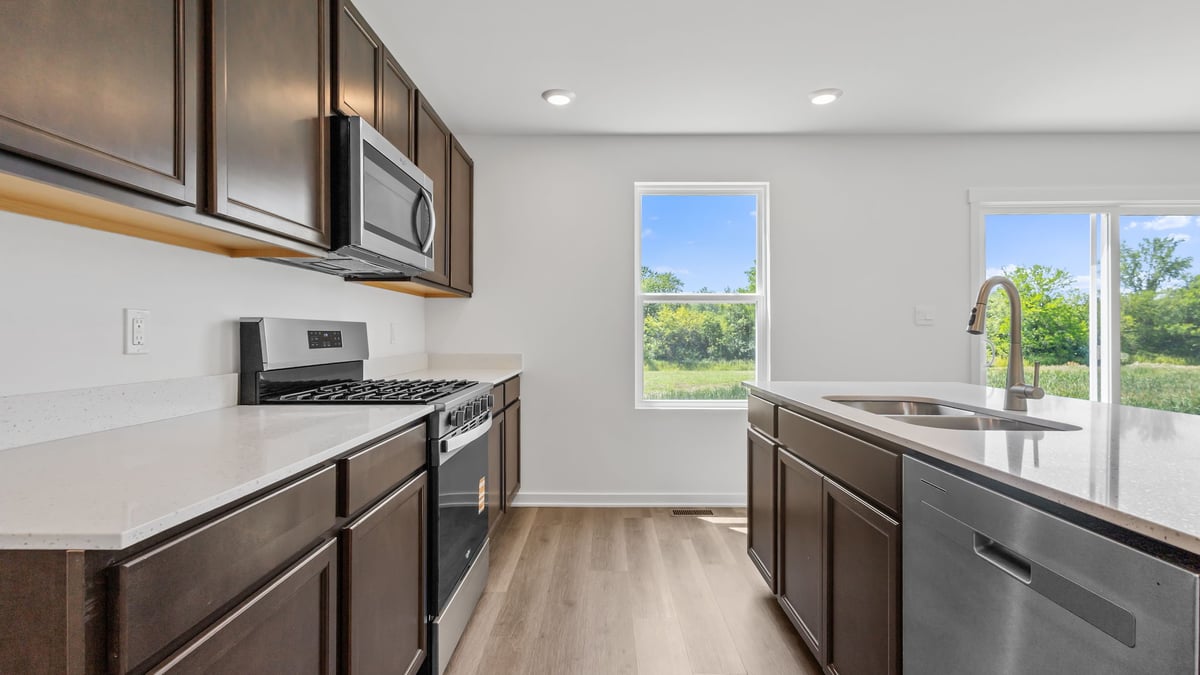 Kitchen with brown cabinetry and view of dining area with window.