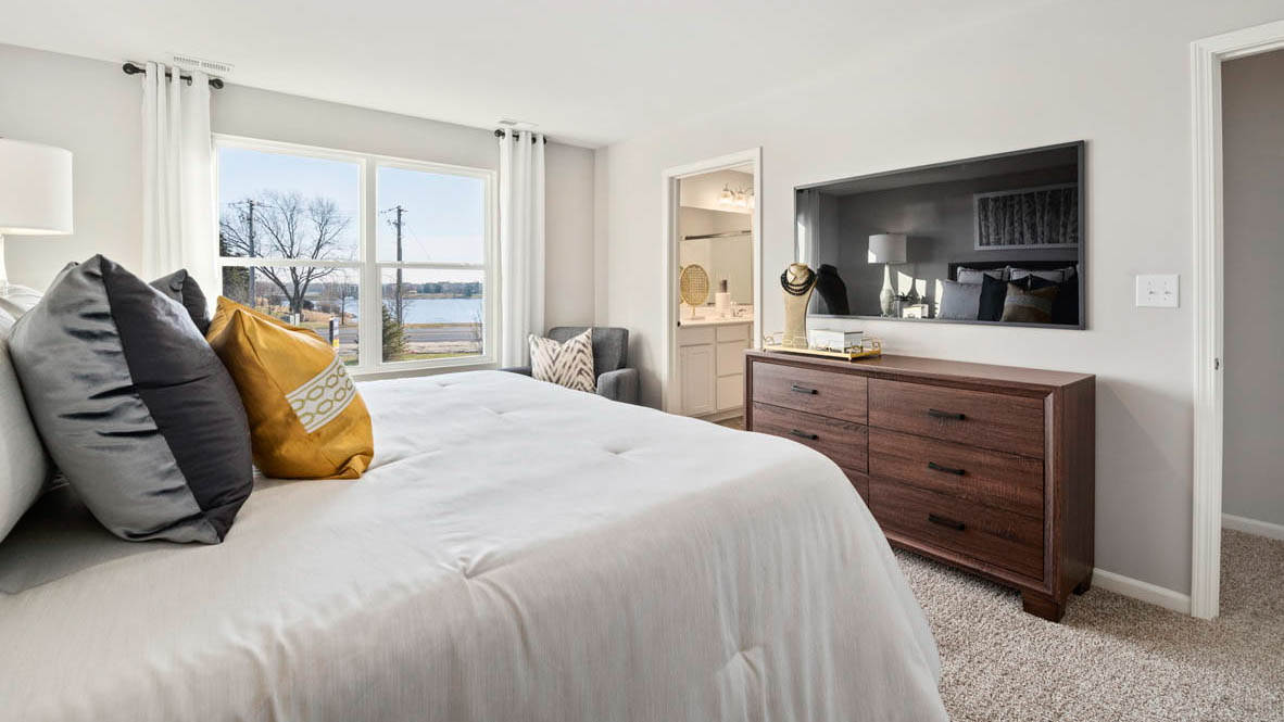 Bedroom featuring a large bed with grey bedding, a dresser, and a large window.