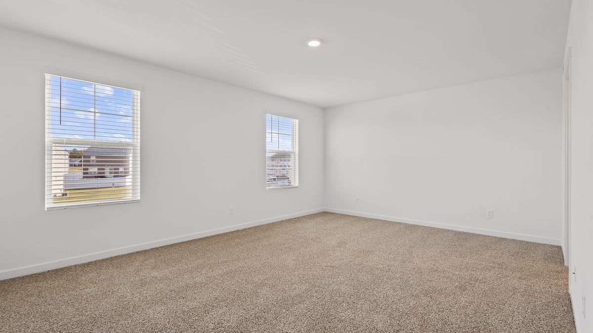 Primary bedroom with two windows and carpeted floors.