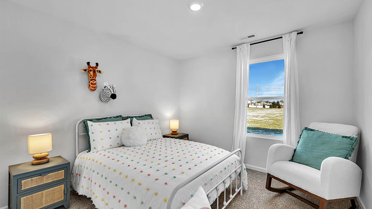 A cozy bedroom with a white bedspread dotted with colorful spots. Animal heads, a giraffe and zebra, decorate the wall. A window shows a sunny landscape.