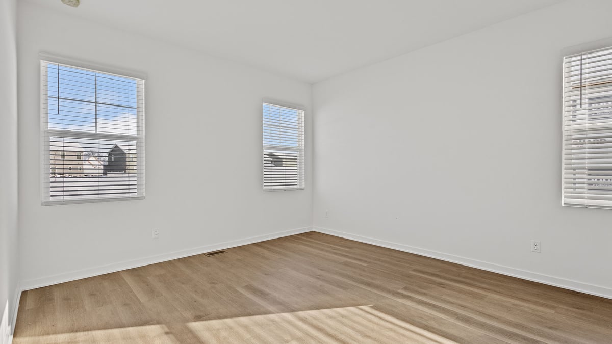 Bedroom with hard wood floors and two windows.