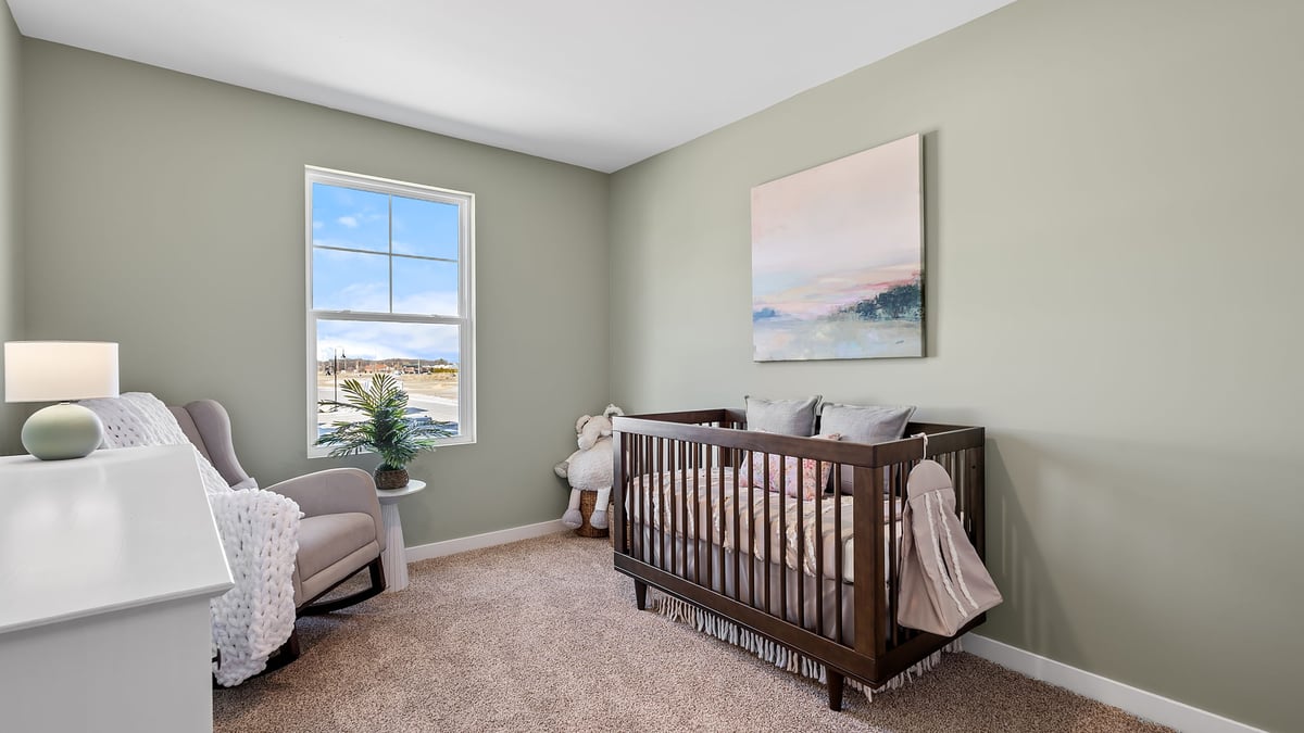 Bedroom staged as a nursery and carpeted floors and a side window.