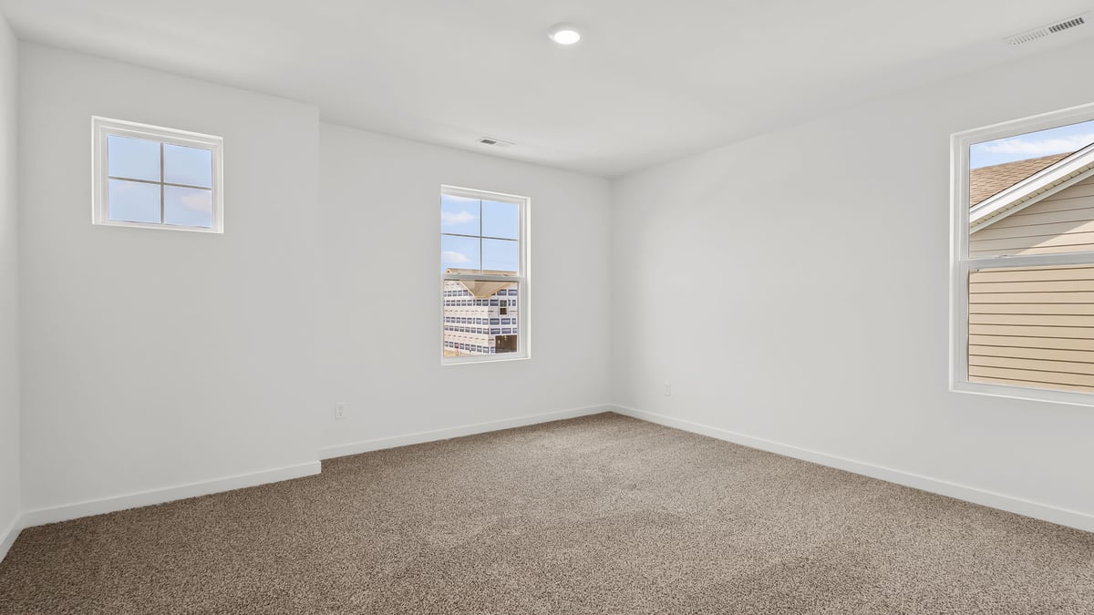 Bedroom with three windows and carpeted floors.