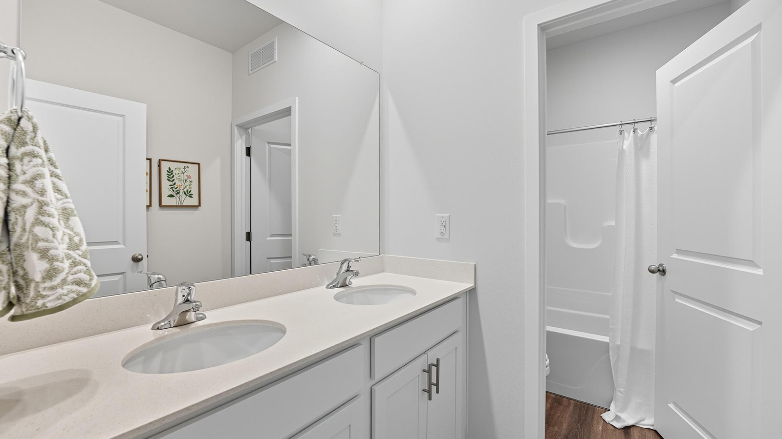 Primary bathroom with double sink vanity, standing glass door shower, and entryway to the walk in closet