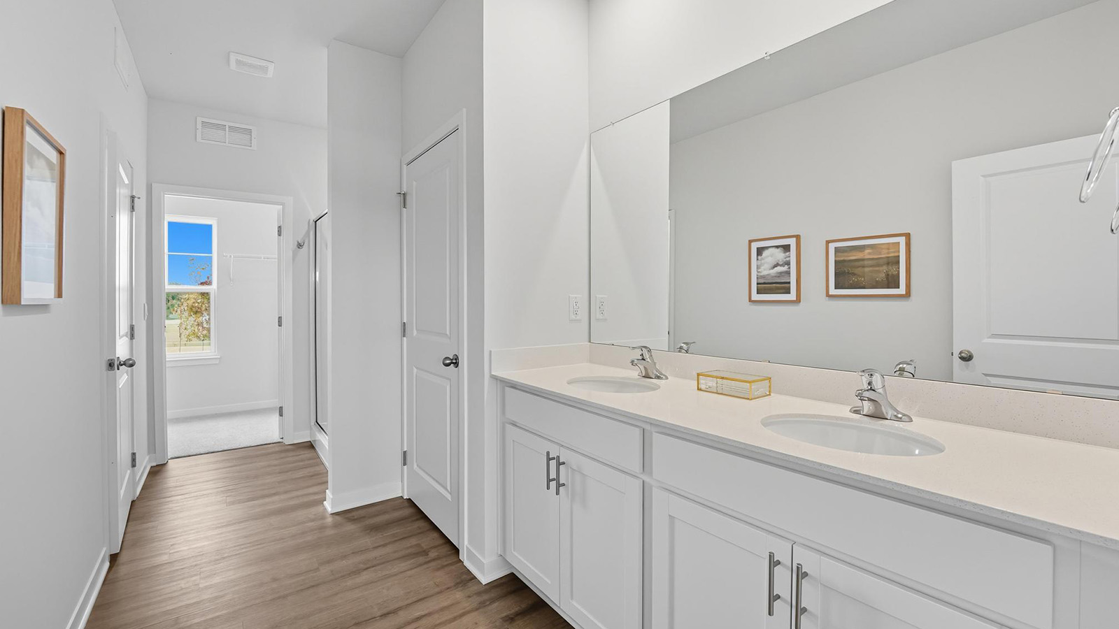 Primary bathroom with double sink vanity, standing glass door shower, and entryway to the walk in closet
