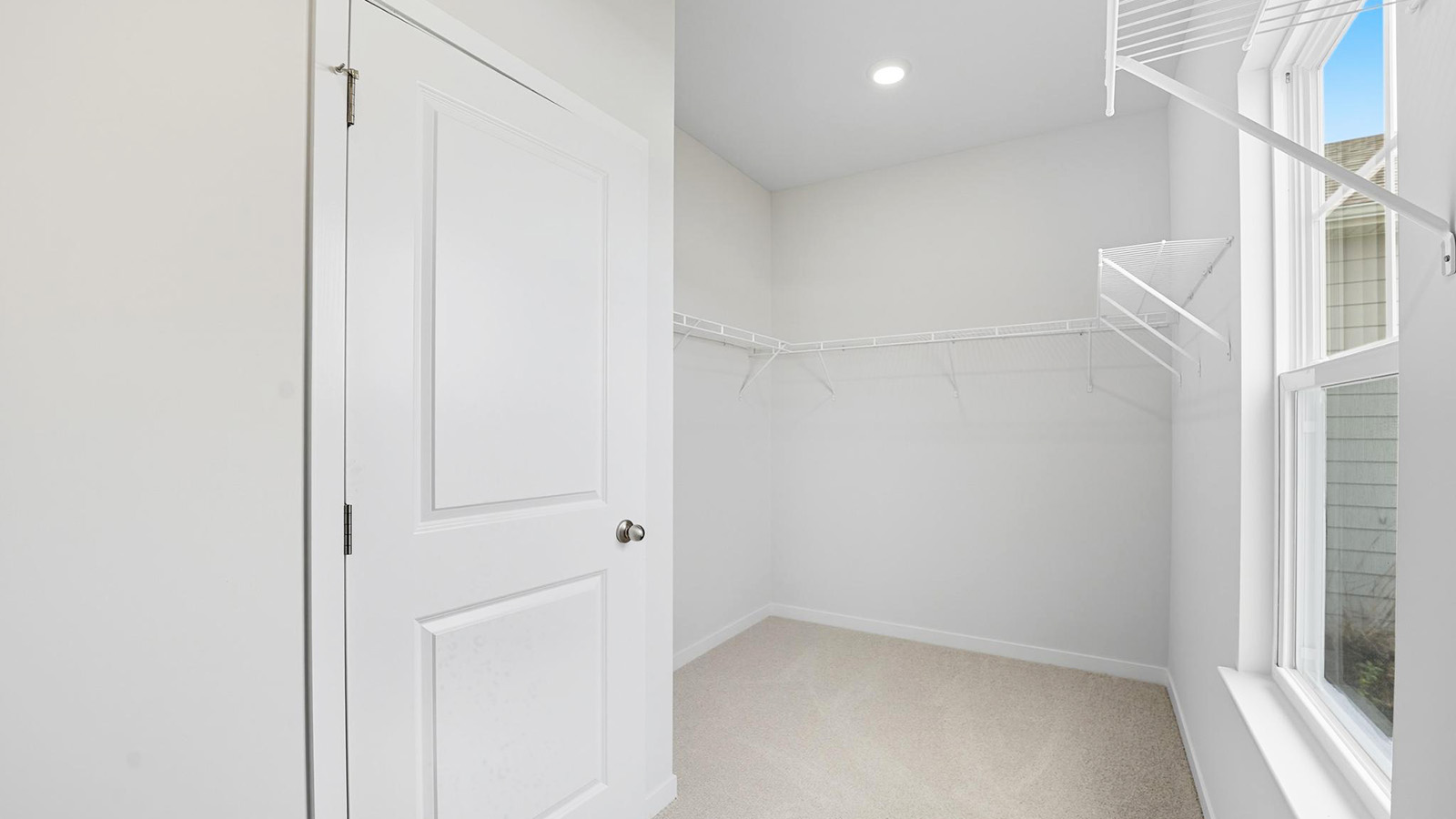 Primary carpeted walk in closet with built in storage racks