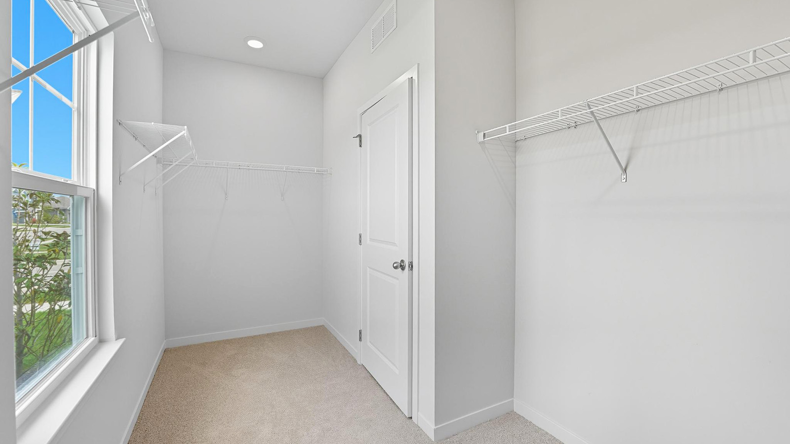 Primary carpeted walk in closet with built in storage racks