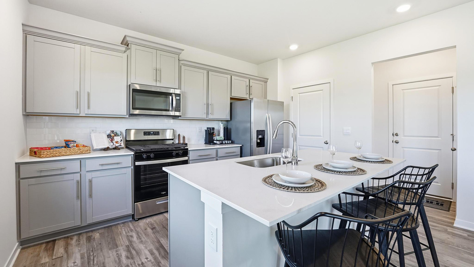 Kitchen and island with white cabinets and stainless steel appliances.