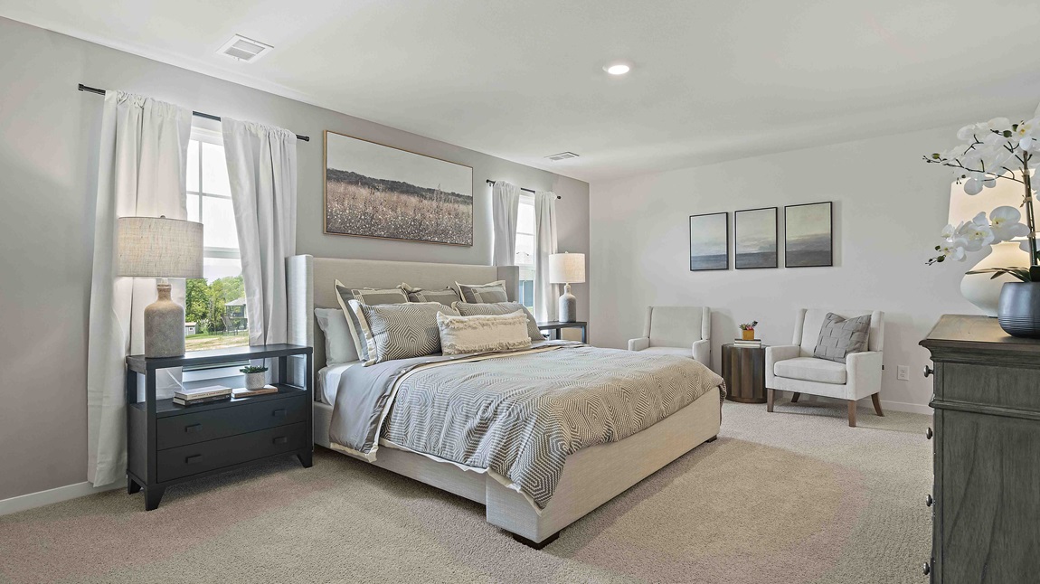 Carpeted primary bedroom with large windows and seating area.