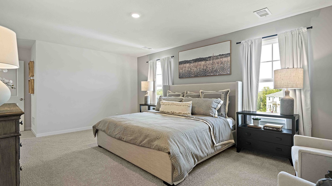 Carpeted primary bedroom with large windows and seating area.