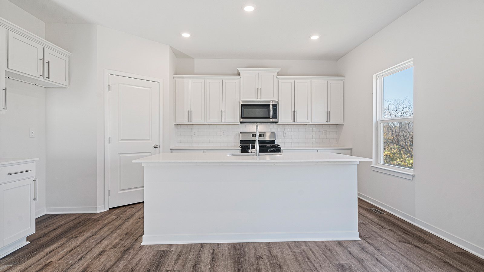 Kitchen and island with white cabinets and stainless steel appliances.