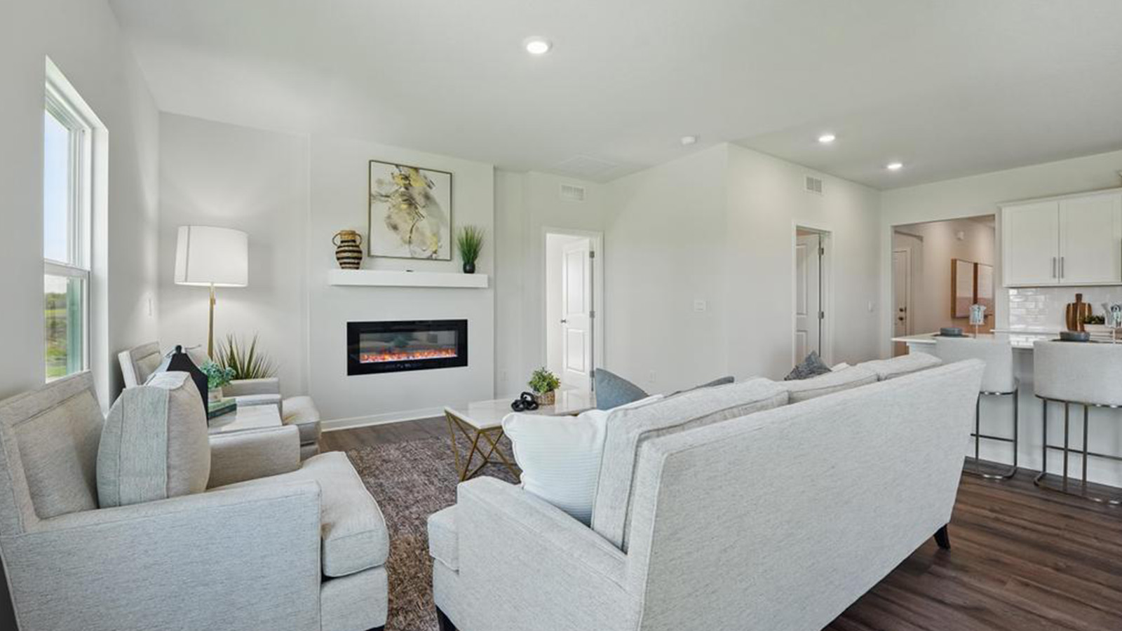 Living room with electric fireplace and two large windows, beside kitchen and dining area.