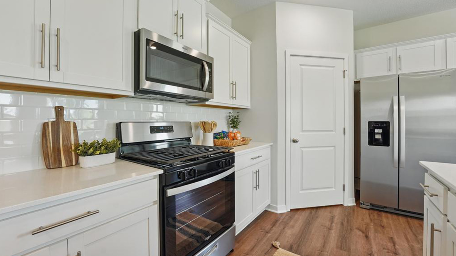 Kitchen and island with white cabinets, subway tile backsplash and stainless steel appliances.