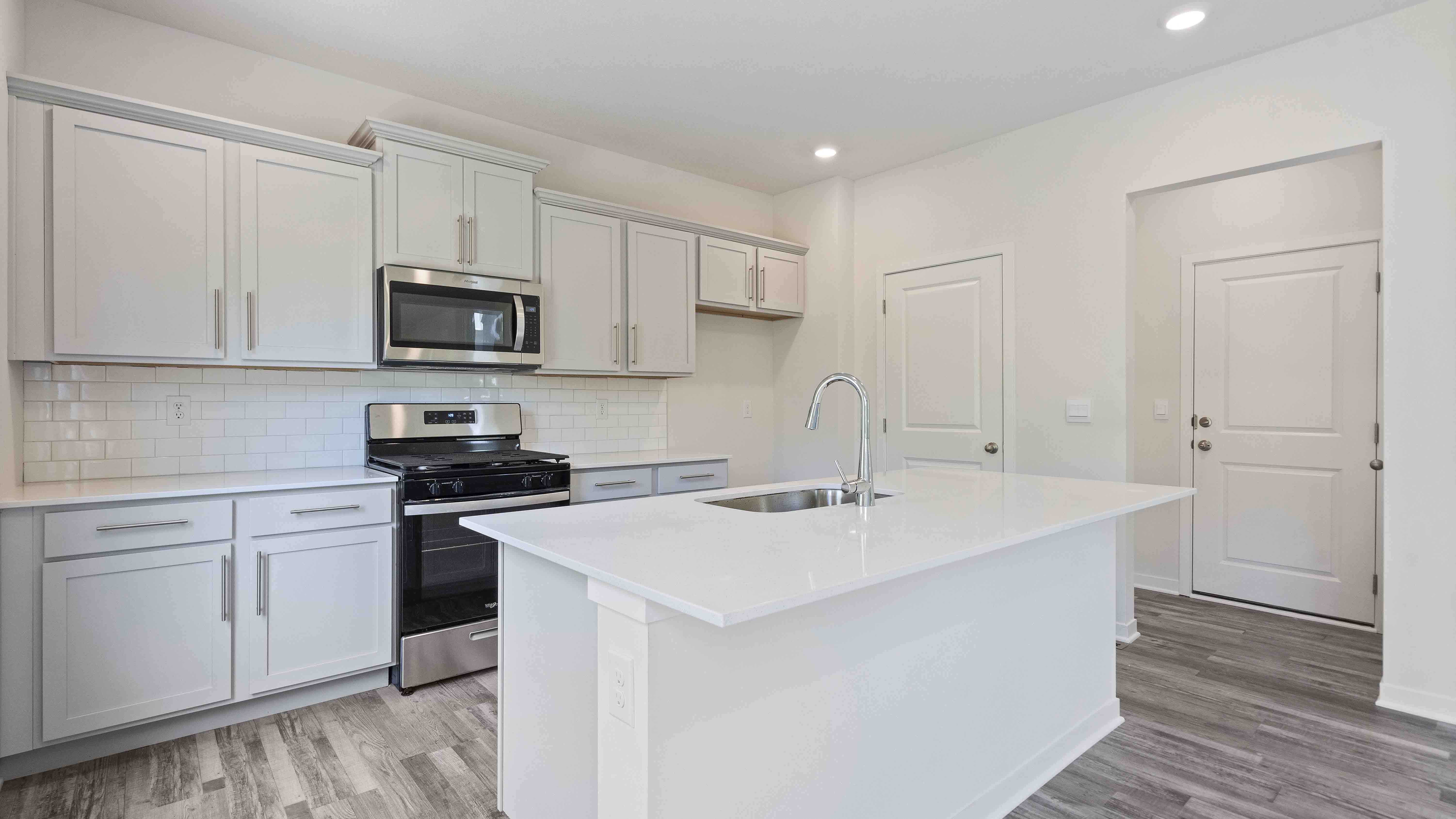 Kitchen and island with white cabinets and stainless steel appliances. New Homes in Kansas City, Missouri