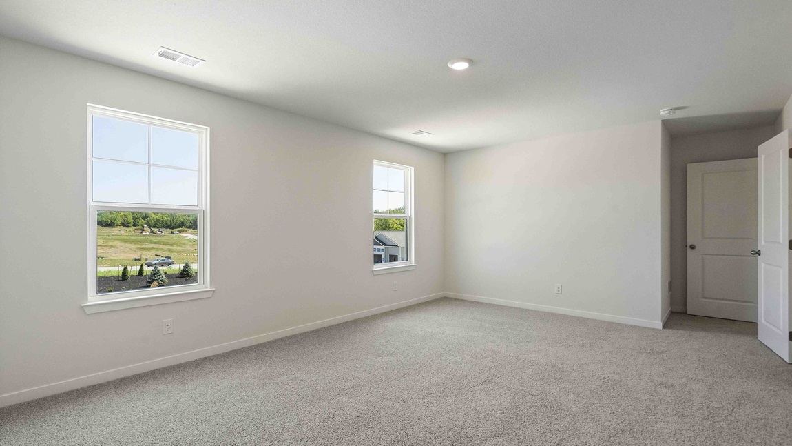 Carpeted primary bedroom with large windows and seating area. New Homes in Kansas City, Missouri