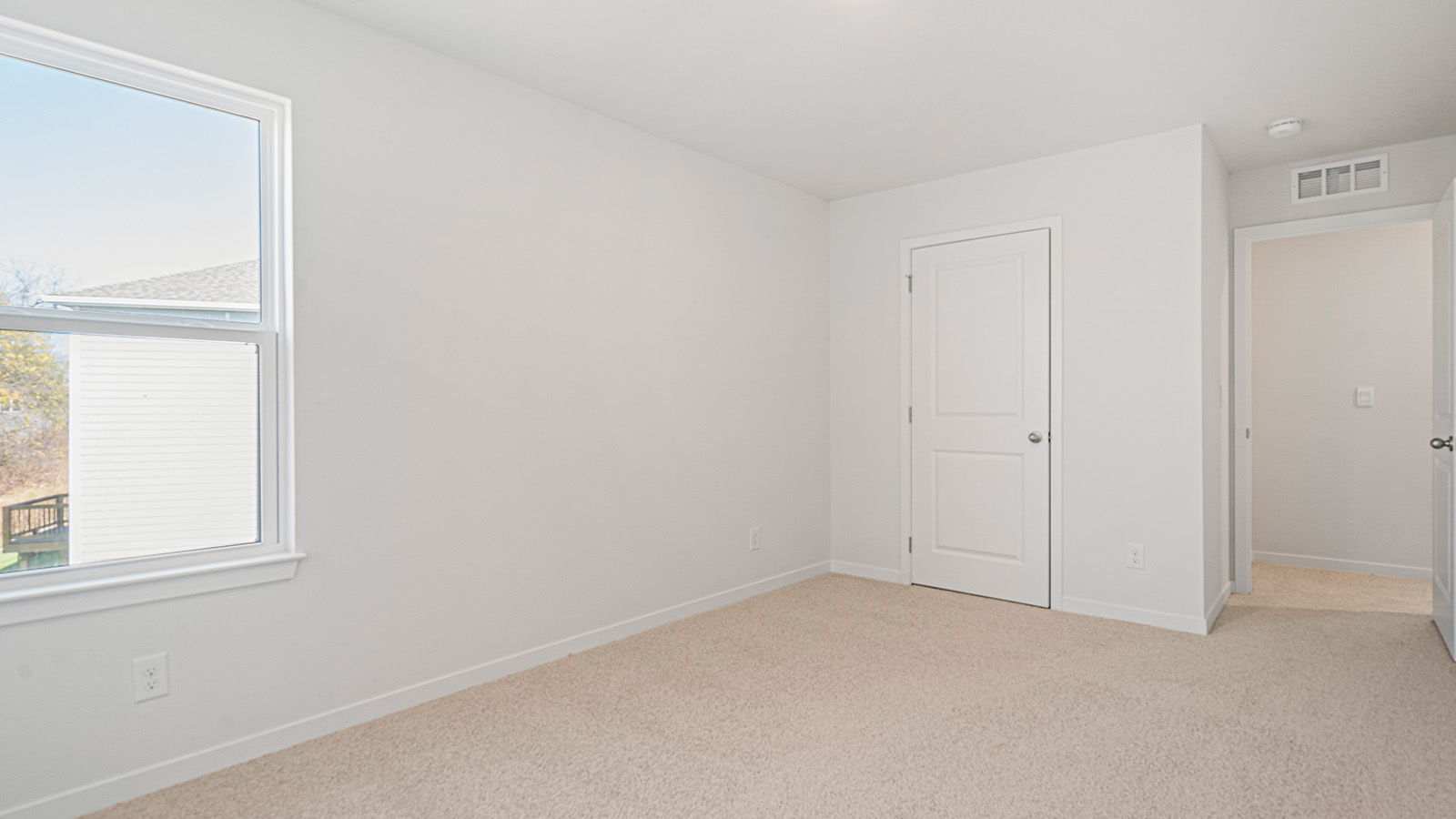 Carpeted primary bedroom with large window.