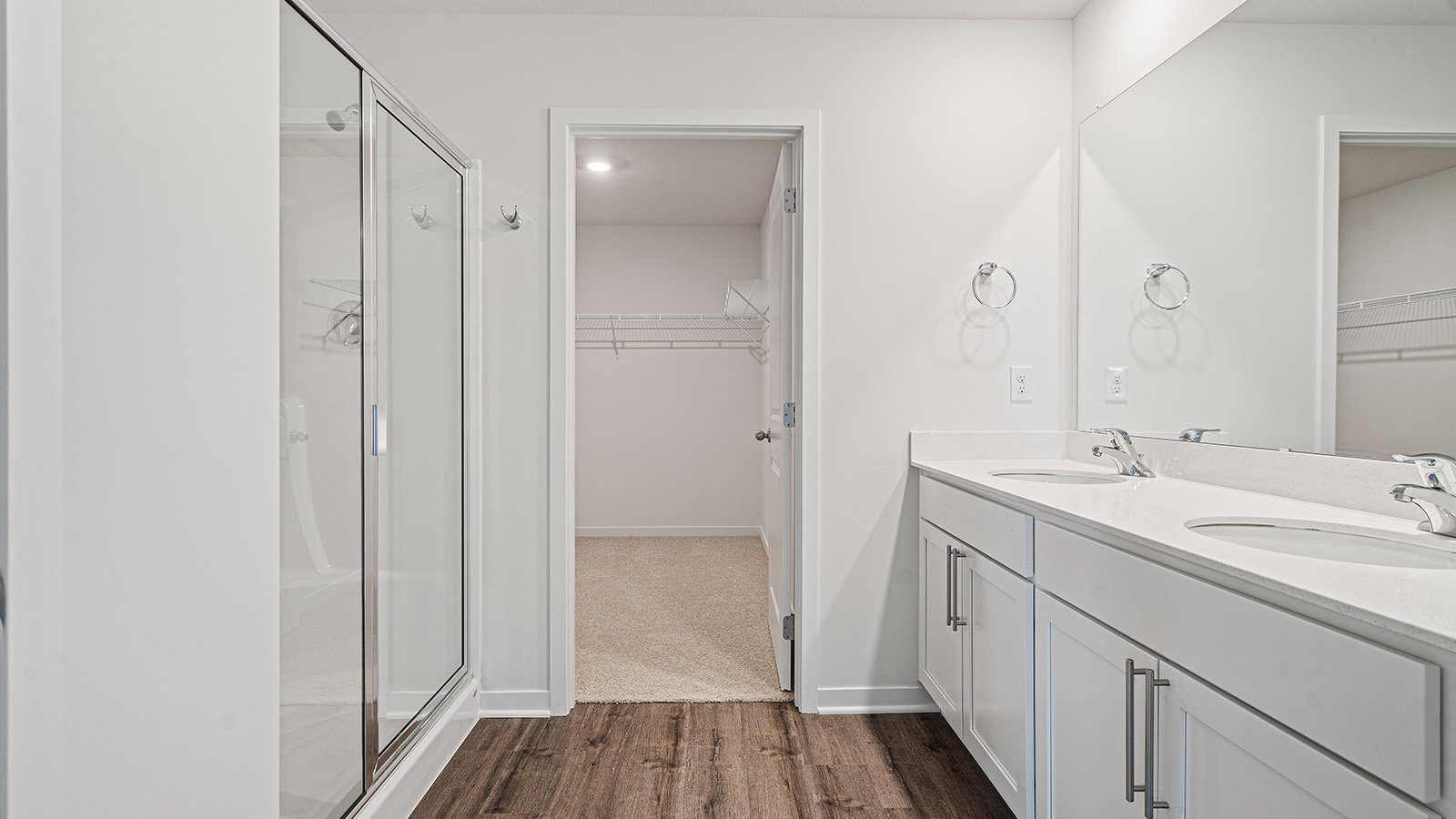 Primary bathroom with double sinks, white cabinets, and glass shower.