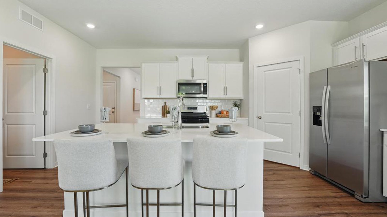 Kitchen and island with white cabinets, subway tile backsplash and stainless steel appliances.