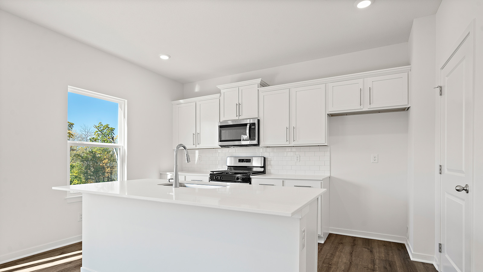 Kitchen and island with white cabinets and stainless steel appliances. New Homes in Kansas City, Missouri