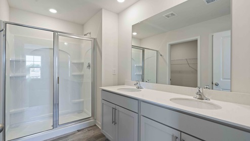 Primary bathroom with double sink vanity, white cabinets and glass door shower