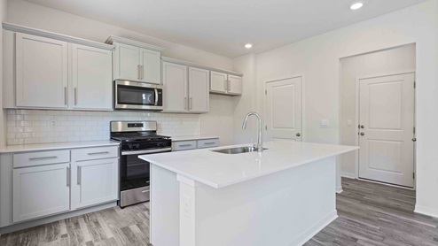 Kitchen and island with white cabinets, tile backsplash, and stainless steel appliances
