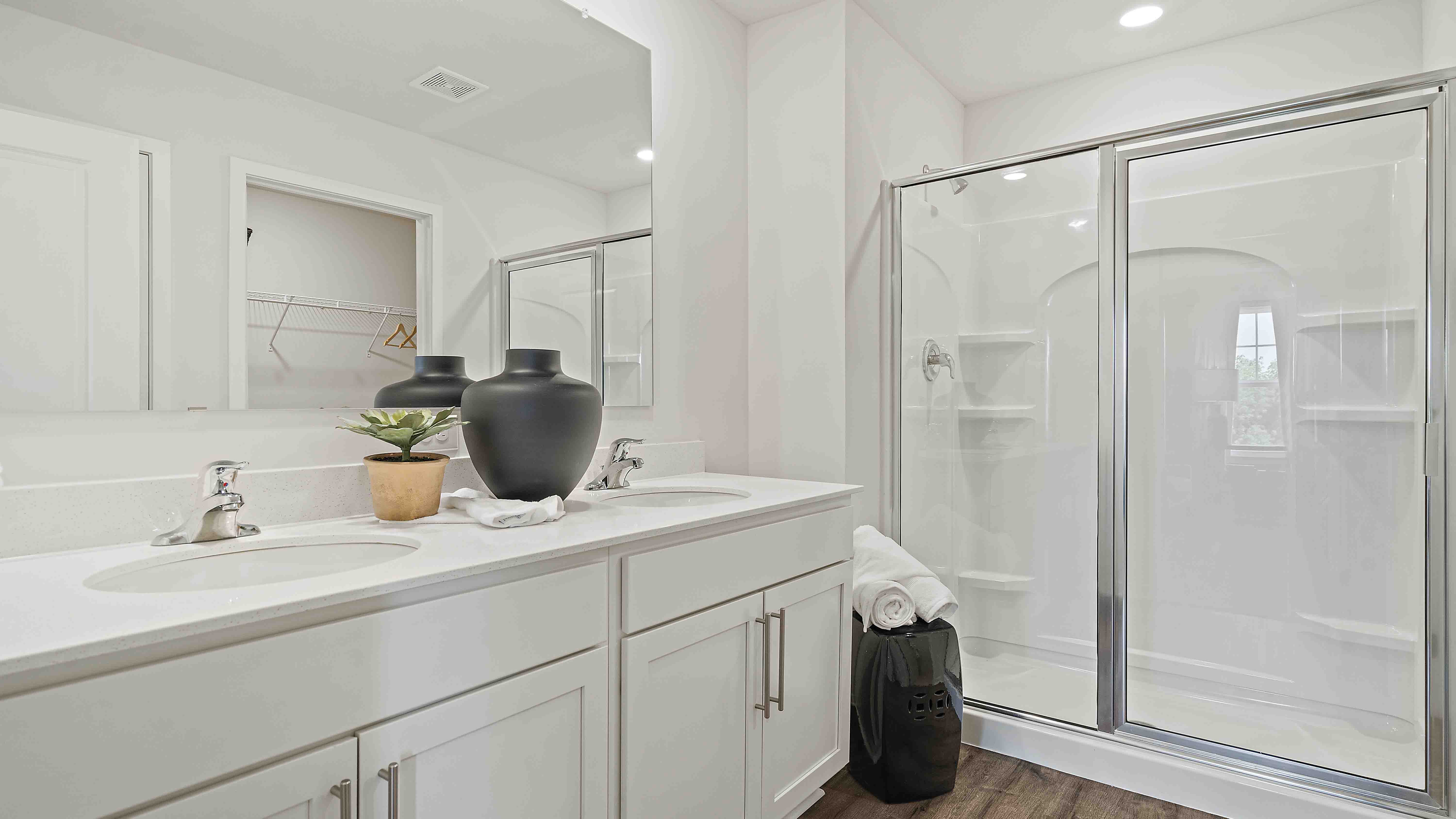 Primary bathroom with double sink vanity, white cabinets and glass door shower