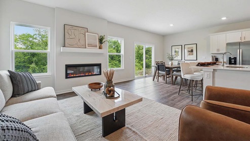 Spacious living room with brown flooring, white walls, a black fireplace and windows