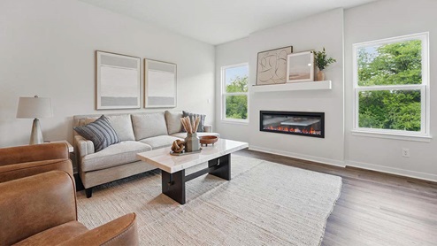 Spacious living room with brown flooring, white walls, a black fireplace and windows