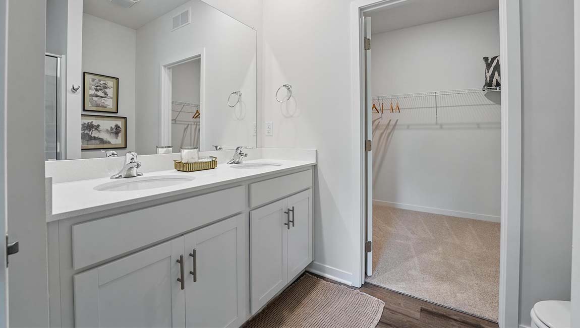 Bathroom with double sink vanity, standing glass door shower, and entryway to the walk in closet