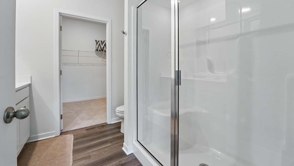 Bathroom with double sink vanity, standing glass door shower, and entryway to the walk in closet