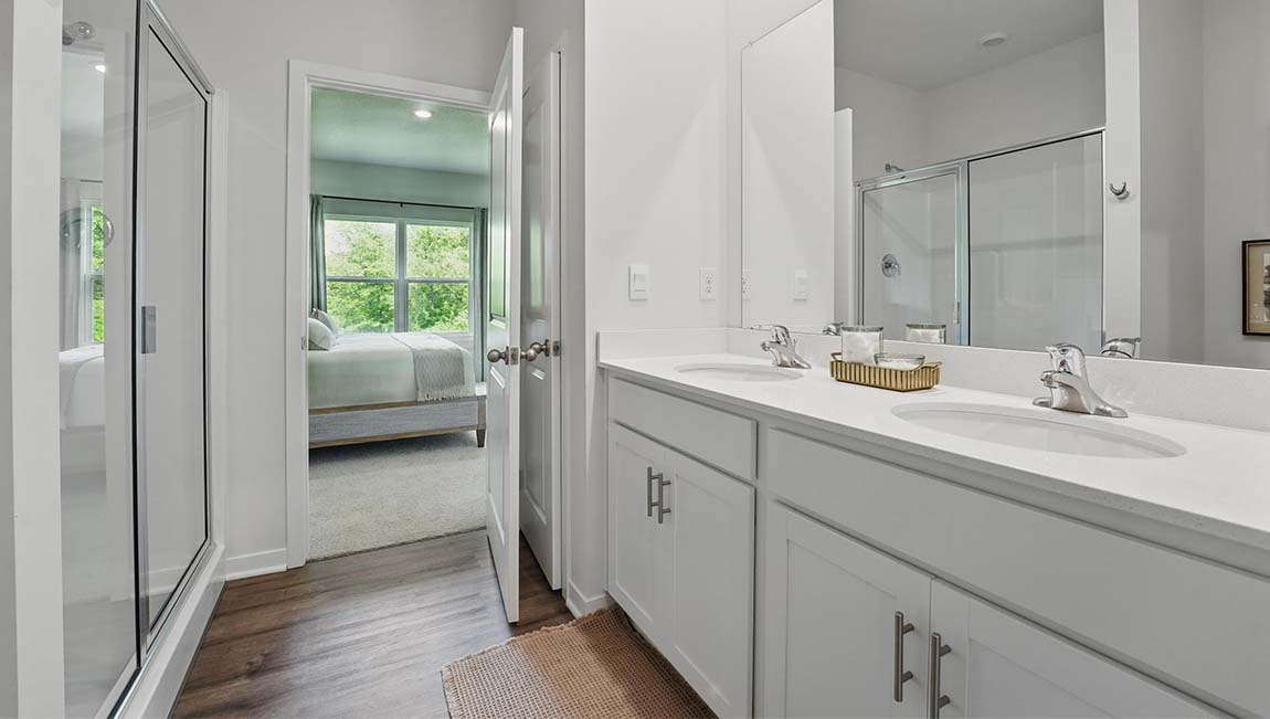 Bathroom with double sink vanity, standing glass door shower, and entryway to the walk in closet