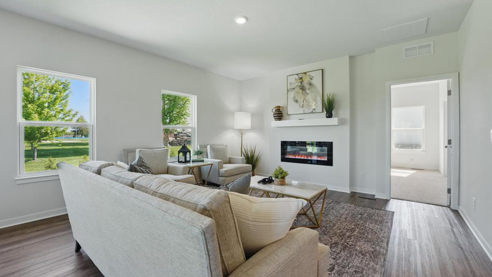 Living room with electric fireplace and two large windows, beside kitchen and dining area.