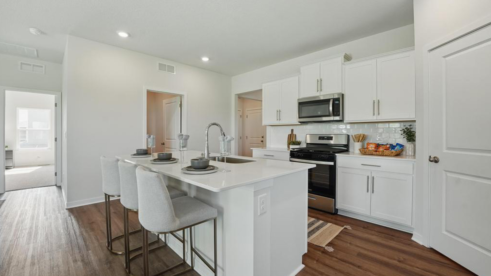 Kitchen and island with white cabinets, subway tile backsplash and stainless steel appliances.