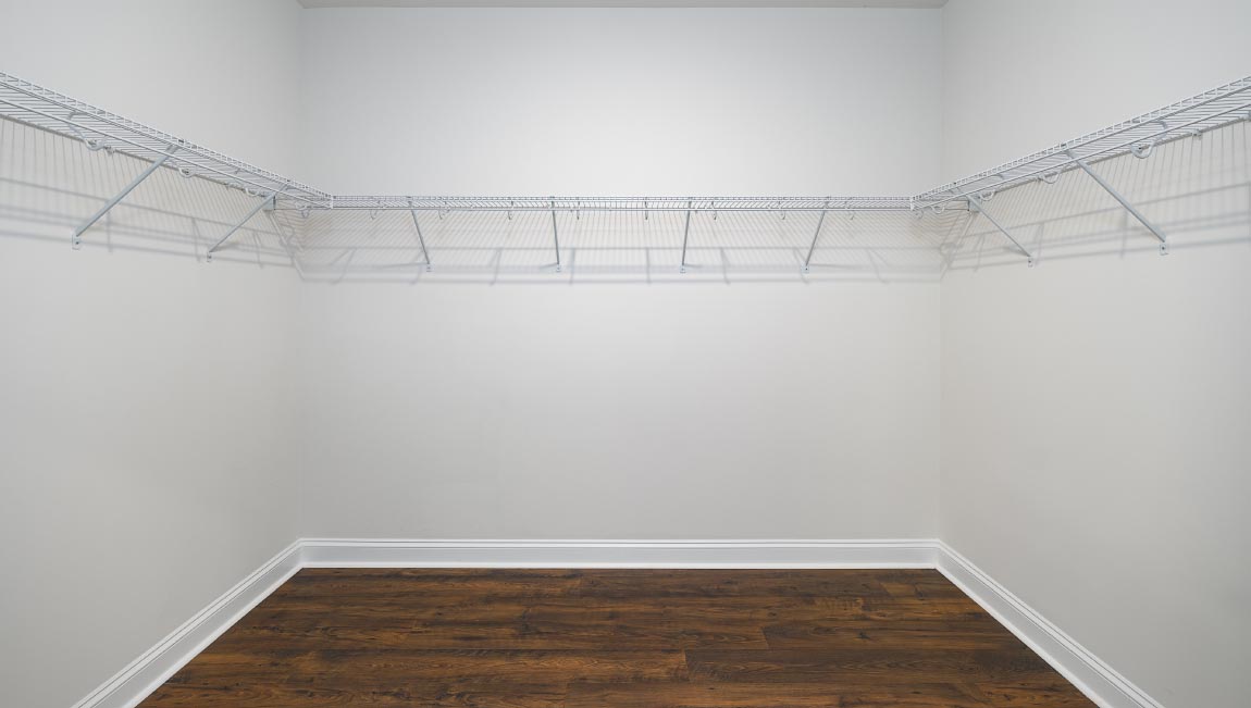 Primary bedroom walk in closet with wood floors and racks for hanging