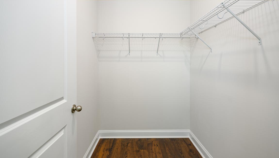 Primary bedroom walk in closet with wood floors and racks for hanging