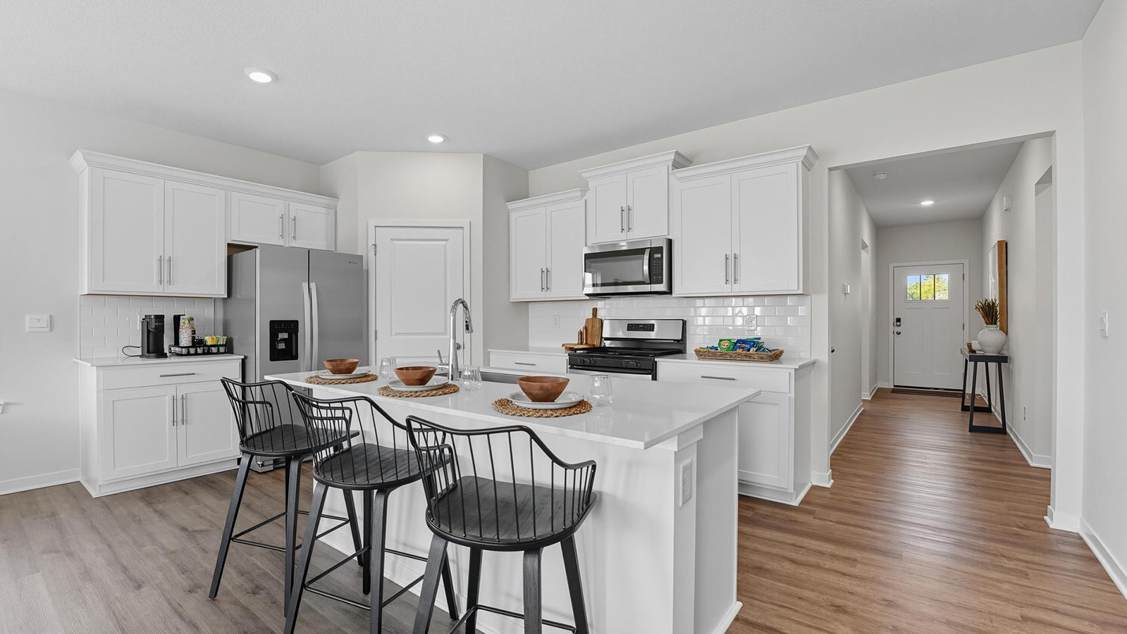 Kitchen and island with white cabinets and stainless steel appliances.